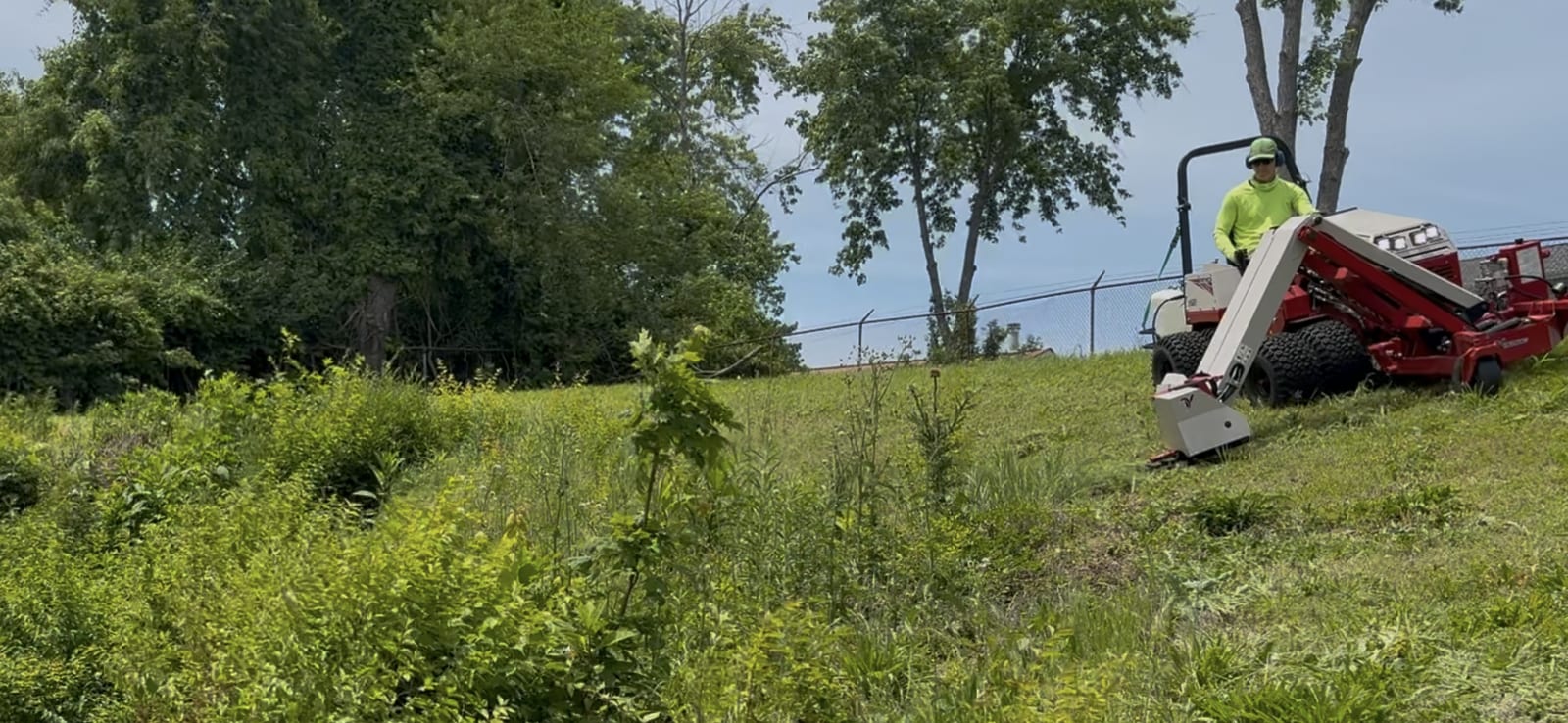 Operator mowing a steep grass embankment beside a commercial property