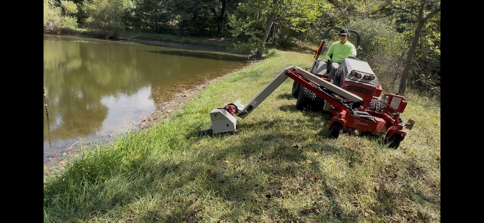 Operator trimming a pond edge with a boom-arm attachment
